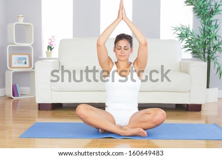Slim brunette woman relaxing sitting in lotus position on exercise mat with hands raised in prayer