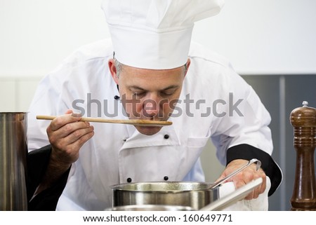 Focused head chef tasting sauce with wooden spoon in professional kitchen