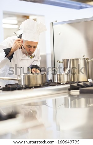 Concentrating head chef tasting food from ladle in professional kitchen