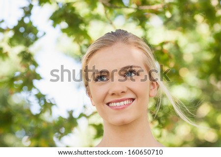Cheerful young woman standing in a park looking away
