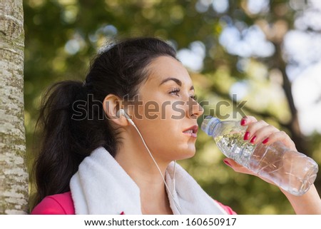Pony tailed brunette woman drinking and leaning against a tree while having a break