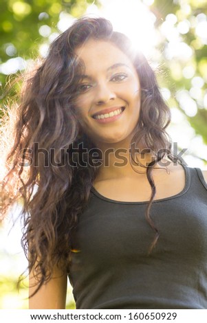 Casual cheerful brunette standing on grass in sunlight in a park on a sunny day
