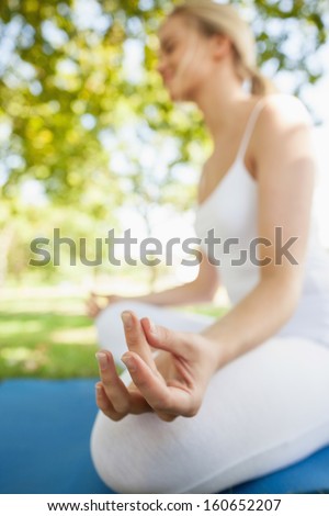 Peaceful young woman sitting on an exercise map meditating in a park