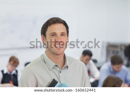 Cute male teacher standing in his classroom smiling at camera