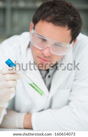 Close-up of a male scientist analyzing green solution in test tube at the laboratory
