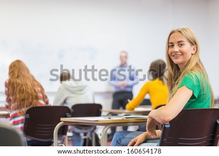 Portrait of a smiling young female student with blurred teachers and others in the classroom