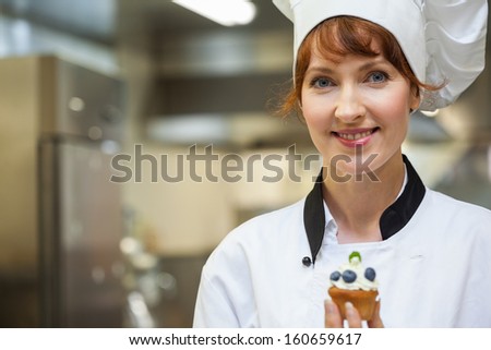 Pretty happy head chef holding blueberry dessert in professional kitchen