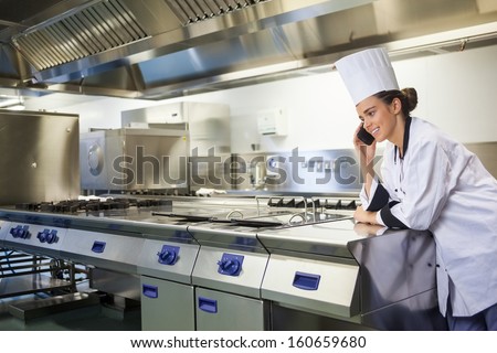 Young happy chef standing next to work surface phoning in professional kitchen