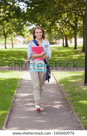 Pretty happy student carrying notebook walking on campus at college
