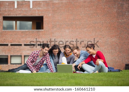 Five Casual Students Sitting On The Grass Pointing At Laptop On Campus At College