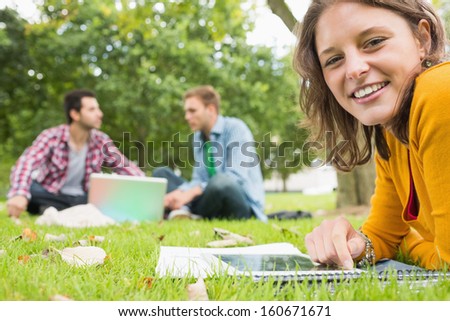Portrait of a young student using tablet PC while two males using laptop in background at the park