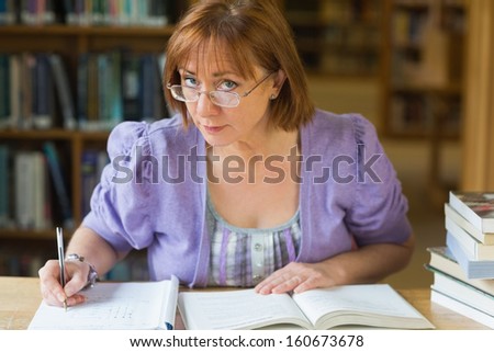 Portrait of a mature female student writing notes at desk in the library