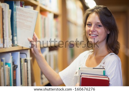 Side view portrait of a smiling young female student selecting book in the library