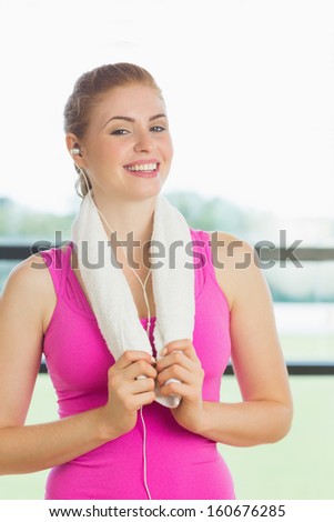 Portrait of a young woman with towel around neck listening to music in fitness studio