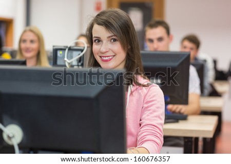Portrait of a smiling female student with others using computers in the college computer room