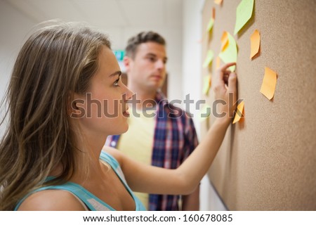 Two students looking at notice board  at college