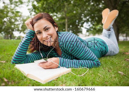 Happy casual student lying on grass listening to music on campus at college at college