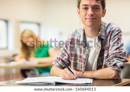 Portrait Of A Smiling Male Student With Others Writing Notes In The Classroom
