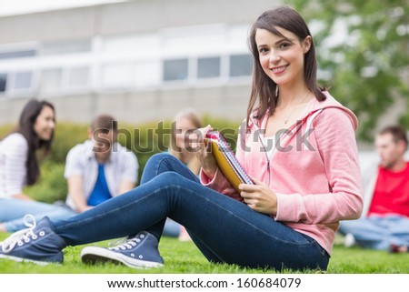 Portrait of a smiling young college student with blurred friends sitting in the park