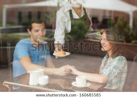 A couple holding hands while waitress serving food in college canteen