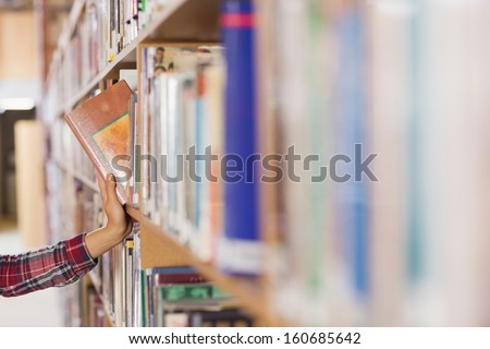 Pretty Student Taking Book Out Of Shelf In Library