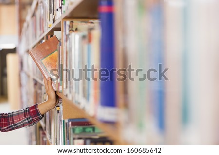 Pretty student taking book out of shelf in library Pretty student taking book out of shelf in library