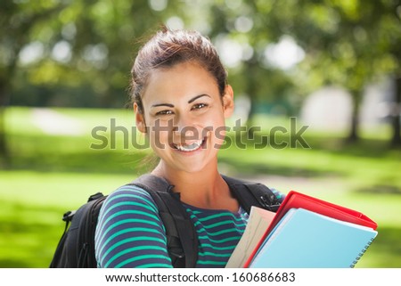 Casual cheerful student holding books on campus at college