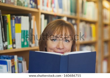 Peaceful mature woman holding a book in a library looking at camera