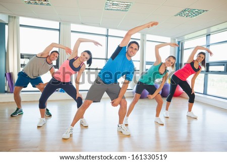 Full length portrait of smiling people doing power fitness exercise at yoga class in fitness studio