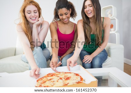 Happy young female friends eating pizza on sofa at home