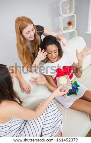 Cheerful young women surprising friend with a gift on sofa at home