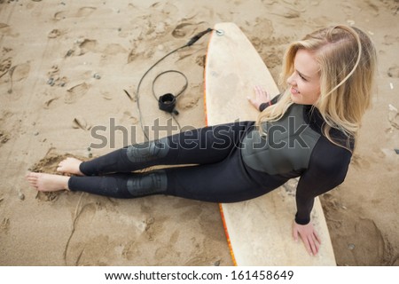 Overhead view of a smiling beautiful blond in wet suit with surfboard at the beach