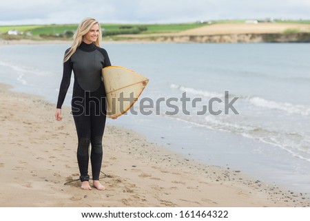 Full length of a beautiful young woman in wet suit holding surfboard at the beach