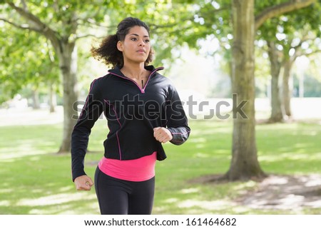Beautiful healthy young woman in black jacket jogging in the park