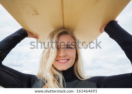 Close up of a smiling young woman in wet suit holding surfboard over head at beach