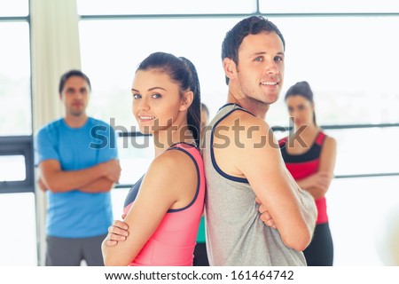 Portrait of a fit couple with friends standing in background in bright exercise room