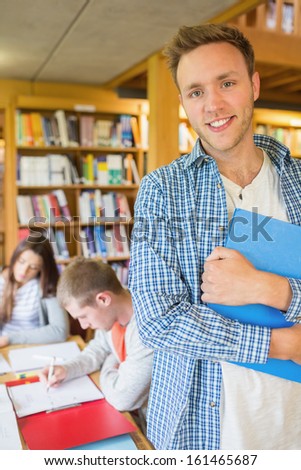 Portrait of a smiling male student with others in background in the college library