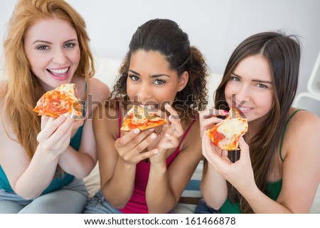 Portrait Of Happy Young Female Friends Eating Pizza On Sofa At Home