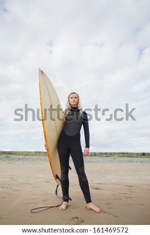 Full length of a beautiful young woman in wet suit holding surfboard at beach