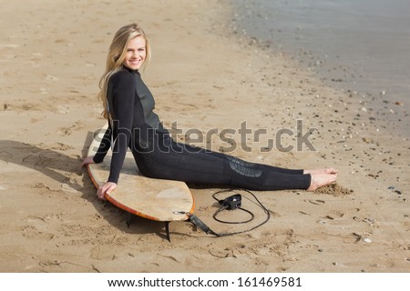 Side view portrait of a beautiful blond in wet suit with surfboard at the beach