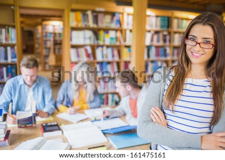 Portrait of a smiling female student with others in background in the college library