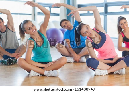 Portrait of fitness class and instructor sitting and stretching hands in bright exercise room