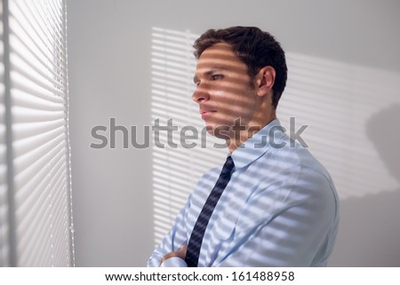 Side view of a young businessman peeking through blinds in office