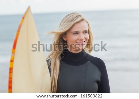 Smiling young woman in wet suit holding surfboard at beach