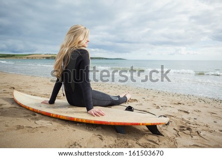 Rear view of a smiling beautiful blond in wet suit with surfboard at the beach