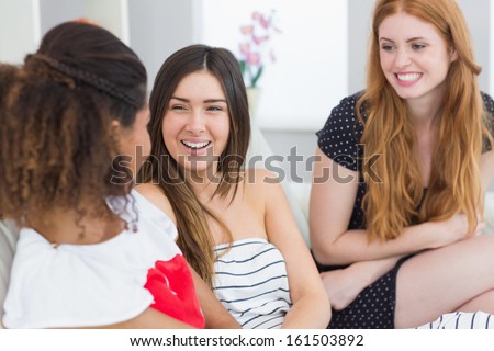 Cheerful young female friends chatting on sofa at home
