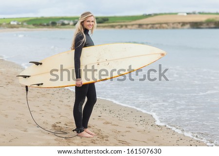 Full length portrait of a beautiful young woman in wet suit holding surfboard at the beach
