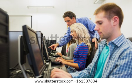 Side view of teacher showing something on screen to student in the computer room