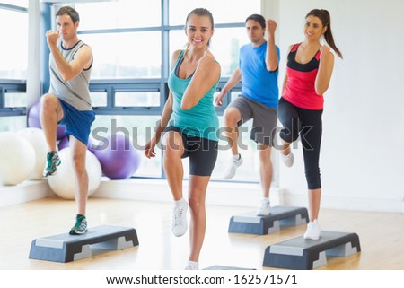 Full length of instructor with fitness class performing step aerobics exercise in gym