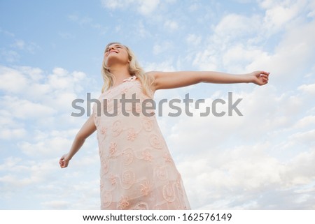 Low angle view of a young woman in summer dress stretching her arms on beach against the sky